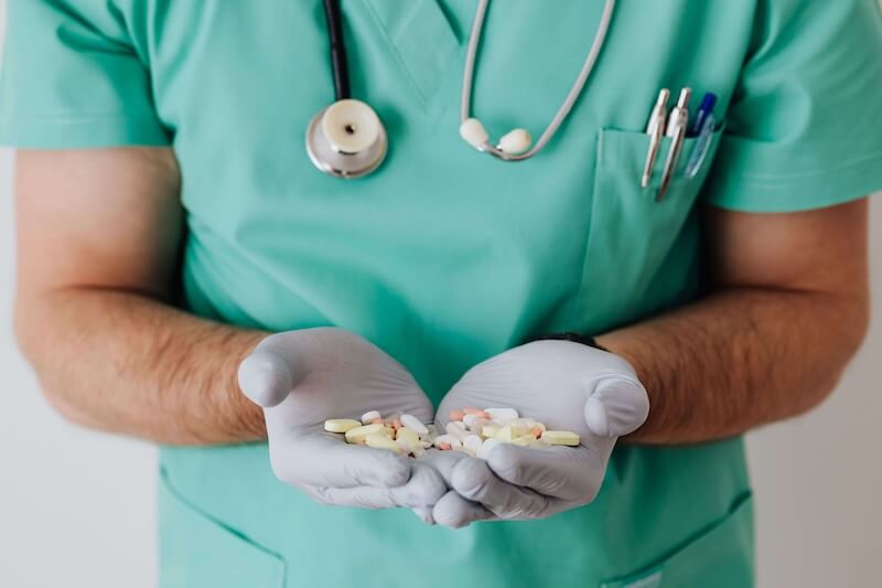 Care worker in teal scrubs holding several medications in gloved hands.