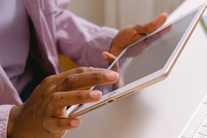 A person in a lilac shirt holding a tablet at a white desk, beside a keyboard and mouse.